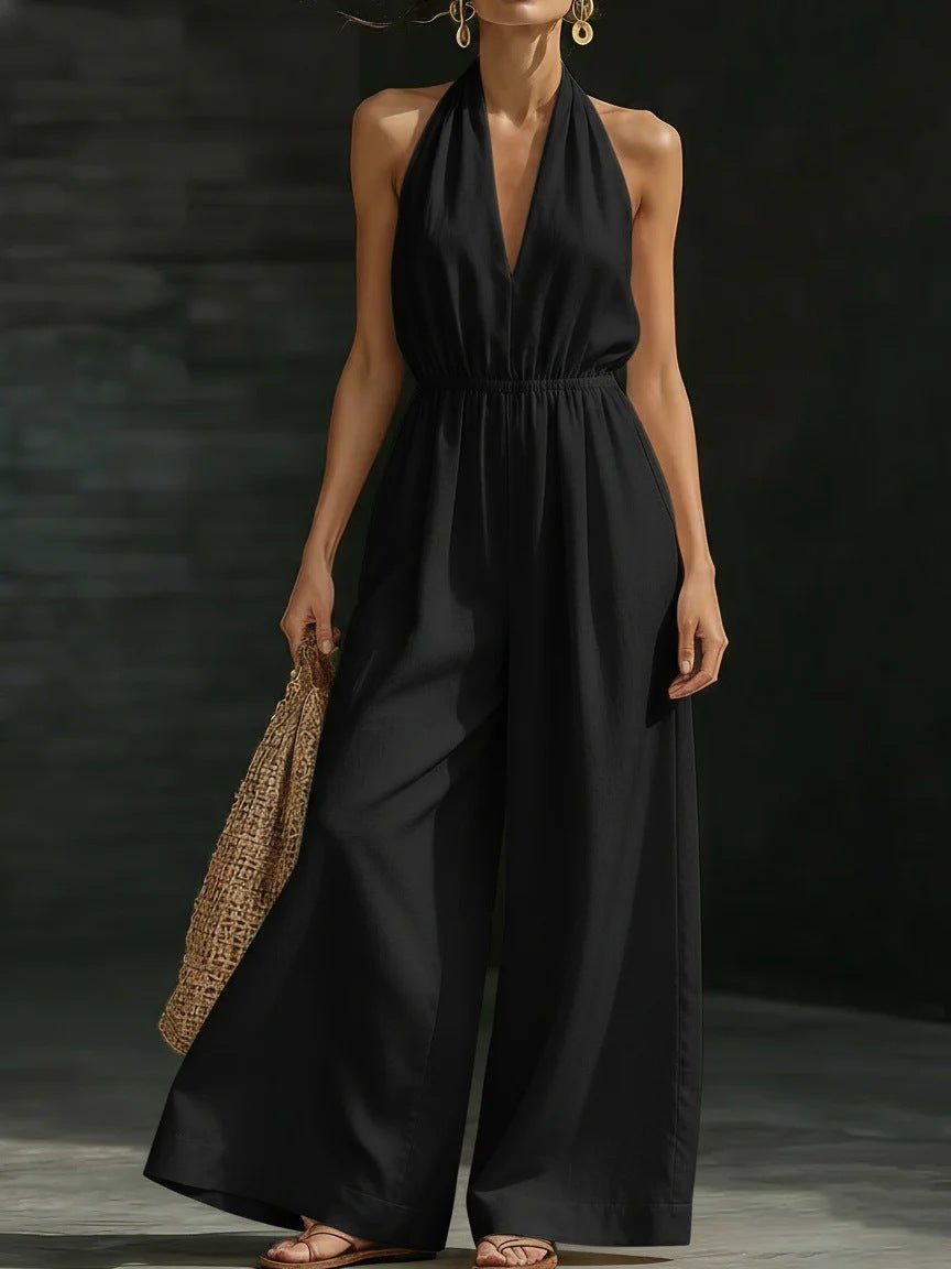 Black halter neck jumpsuit with wide legs, elastic waist, and deep V-neck, paired with woven bag and sandals